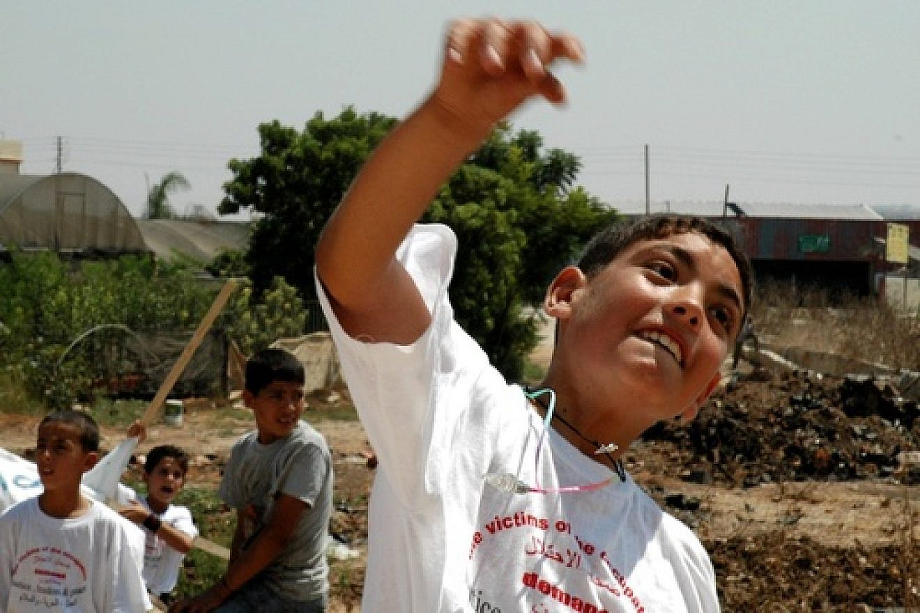 Click photo to download. Caption: A Palestinian boy throws a stone at Israel's security fence. Credit: Justin McIntosh via Wikimedia Commons
