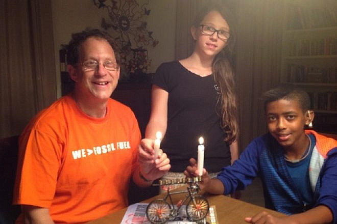 Solar-power pioneer Yosef Abramowitz (left) pictured with two of his five children, Ashira and Zamir, as the family uses its bicycle-shaped Hanukkah menorah. Credit: Courtesy Yosef Abramowitz.