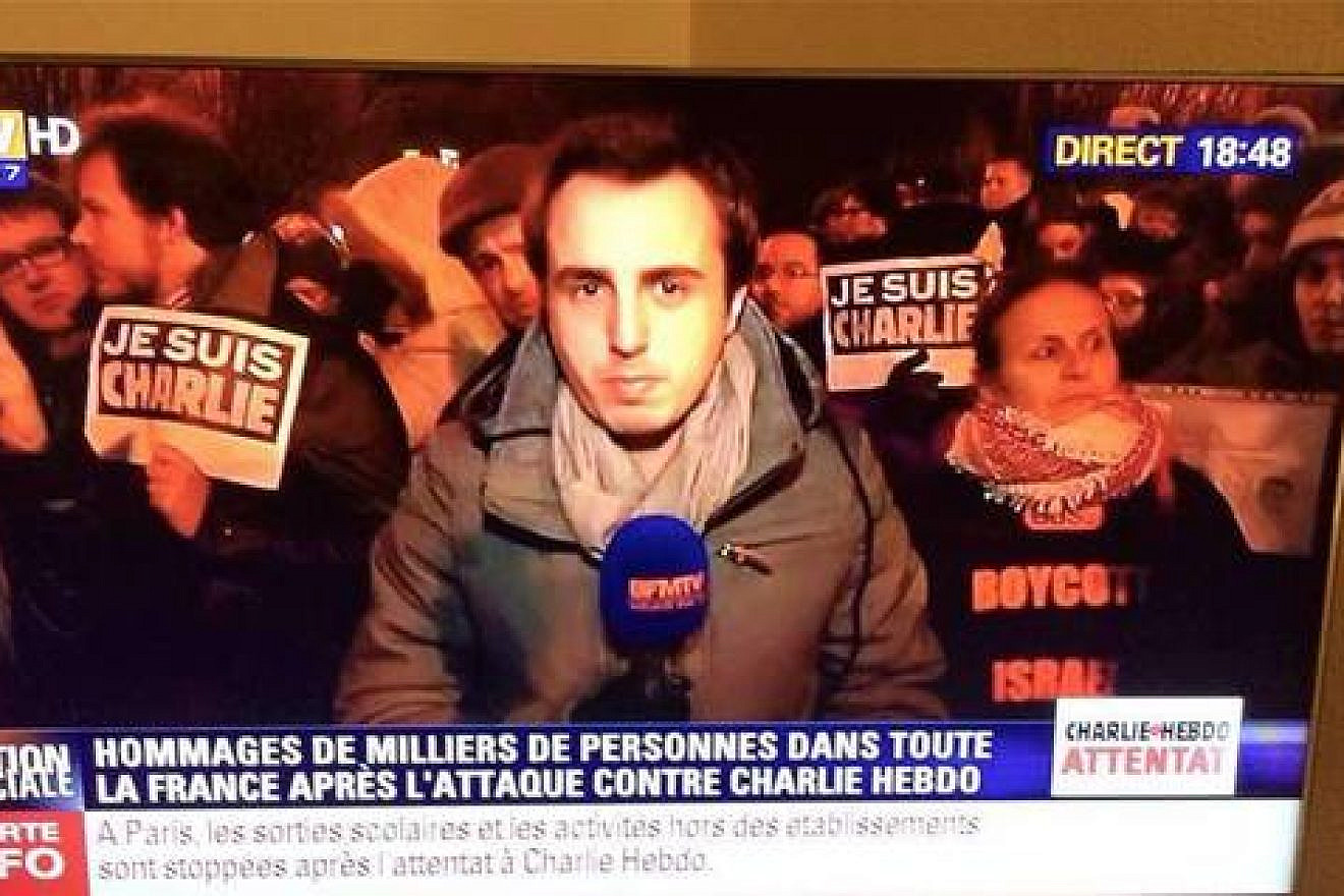 In this image circulating on social media depicts a news report from the scene of a mourners’ rally for the murdered Charlie Hebdo journalists, a woman (pictured on the right) behind the reporter is seen wearing a shirt with the wording “Boycott Israel,” seemingly making the statement that Israel is somehow to blame for the attack on the magazine. Credit: Facebook.