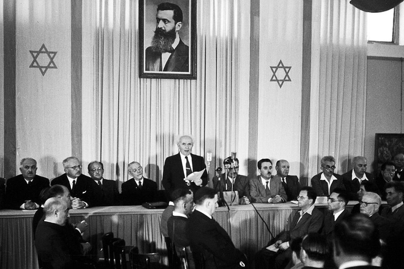Israeli founding father and first prime minister David Ben-Gurion declares independence beneath a portrait of Theodor Herzl, the founder of modern Zionism, at the Tel Aviv Museum (today, Independence Hall) on May 14, 1948. Credit: Wikimedia Commons.