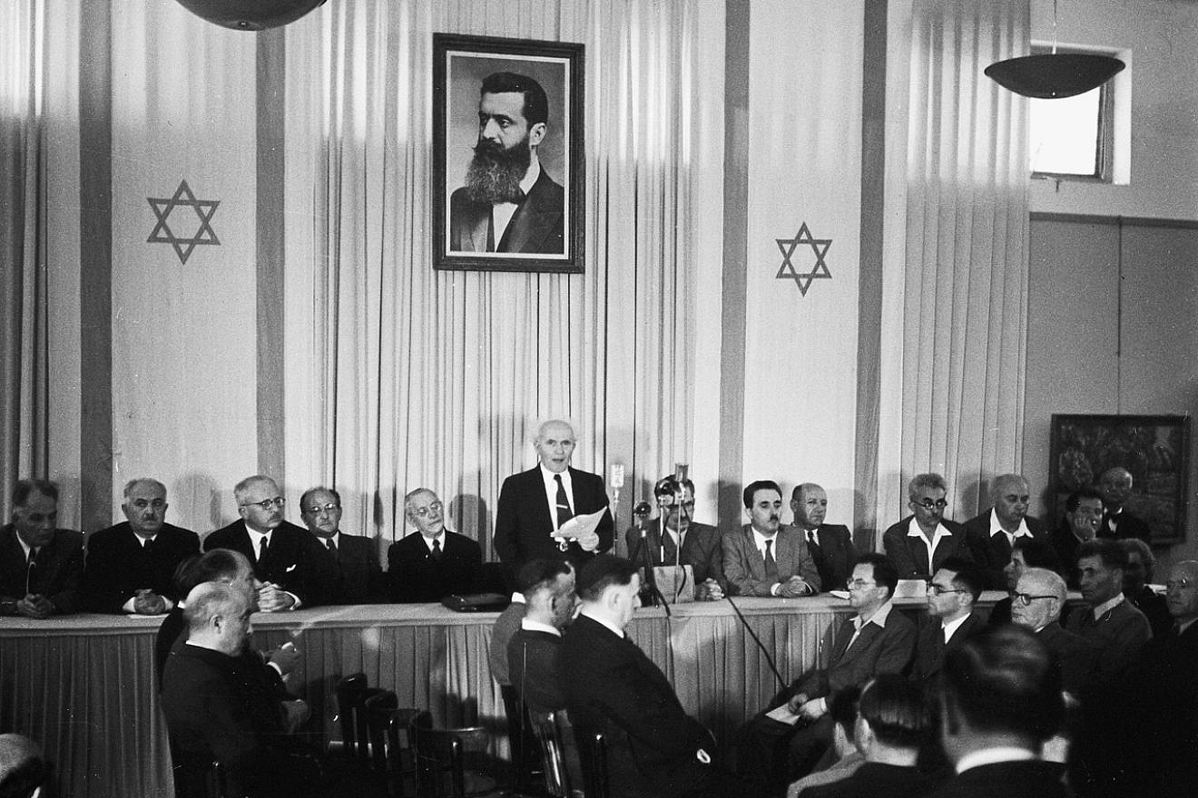 Israeli founding father and first prime minister David Ben-Gurion declares independence beneath a portrait of Theodor Herzl, the founder of modern Zionism, at the Tel Aviv Museum (today, Independence Hall) on May 14, 1948. Credit: Wikimedia Commons.