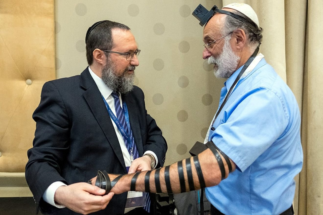 Rabbi Ephraim Mintz, director of the Rohr Jewish Learning Institute, wraps tefillin with Robert Meeropol, 71, the son of convicted and executed U.S. spies Julius and Ethel Rosenberg. Credit: Photo by Mendy Moskowitz/JLI.