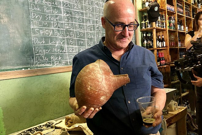 Professor Aren Maeir, from Bar-Ilan University’s Land of Israel studies and archaeology, models an ancient vessel and the new, recreated beer. Credit: Eliana Rudee.