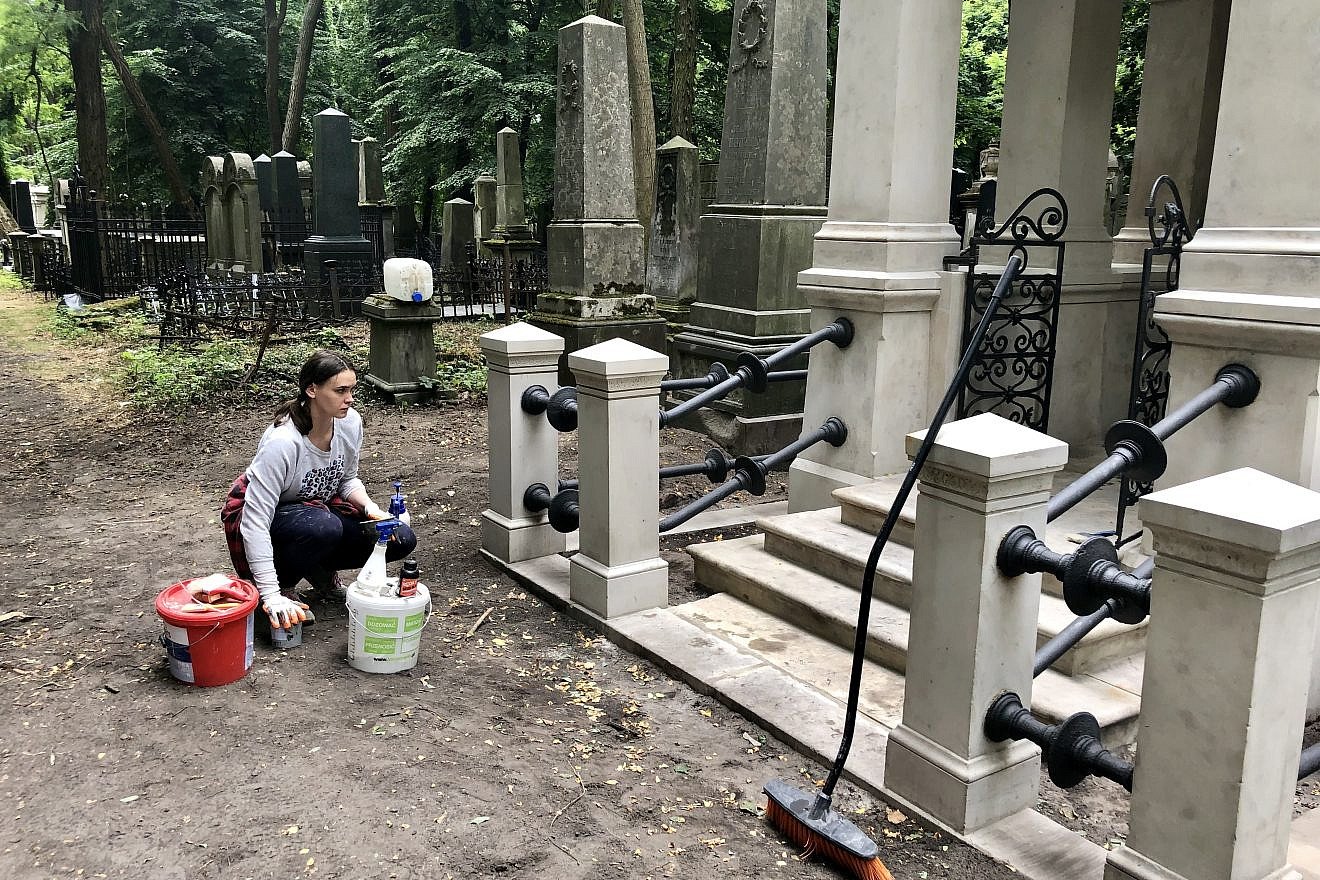 A woman cleans a tomb at Warsaw’s Jewish cemetery, July 2019. Photo by Eliana Rudee.