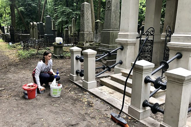 A woman cleans a tomb at Warsaw’s Jewish cemetery, July 2019. Photo by Eliana Rudee.