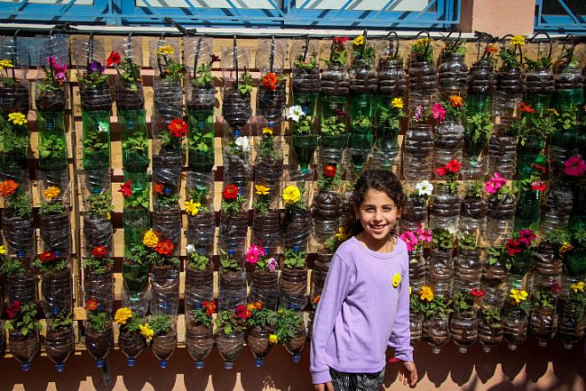 A girl stands by a wall full of flowers in plastic bottles at Amichai School in Kibbutz Yavne on March 24, 2017. Photo by Gershon Elinson/Flash90.