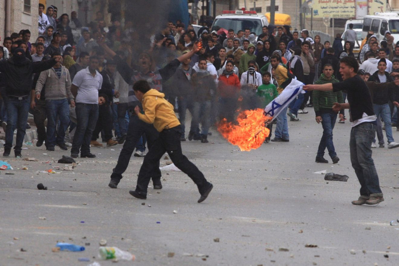 Palestinians burn an Israeli flag during a “Day of Rage” riot at Qalandiya checkpoint near Ramallah in the West Bank, March 16, 2010. Photo by Issam Rimawi/Flash90.