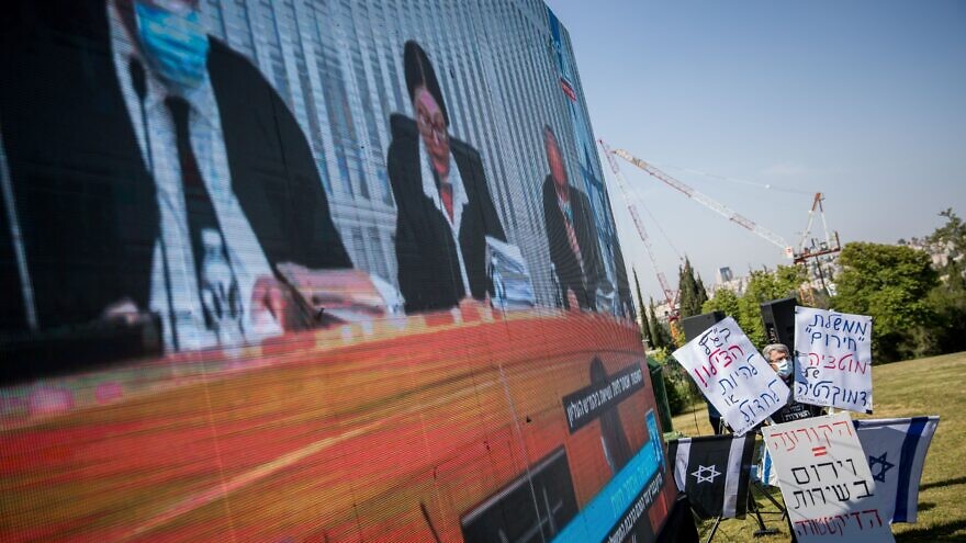Israelis watch a Supreme Court session on petitions filed against the proposed government outside the Knesset, April 3, 2020. Photo by Yonatan Sindel/Flash90.