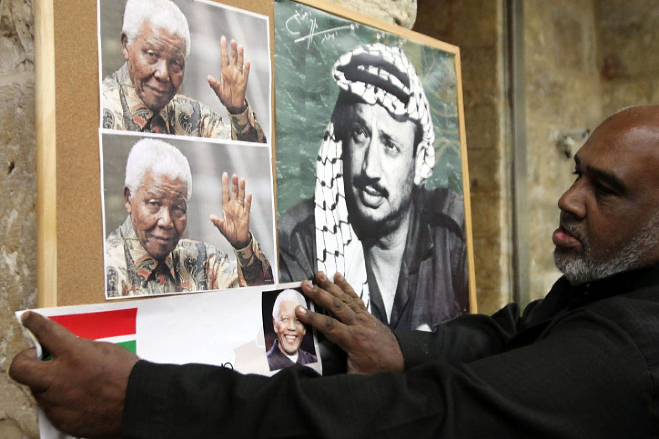 An Arab man hangs a picture of former South African leader Nelson Mandela next to a poster of former PLO chief Yasser Arafat, at a memorial service for Mandela in Jerusalem's Old City, Dec. 8, 2013. Photo by Sliman Khader/Flash90.