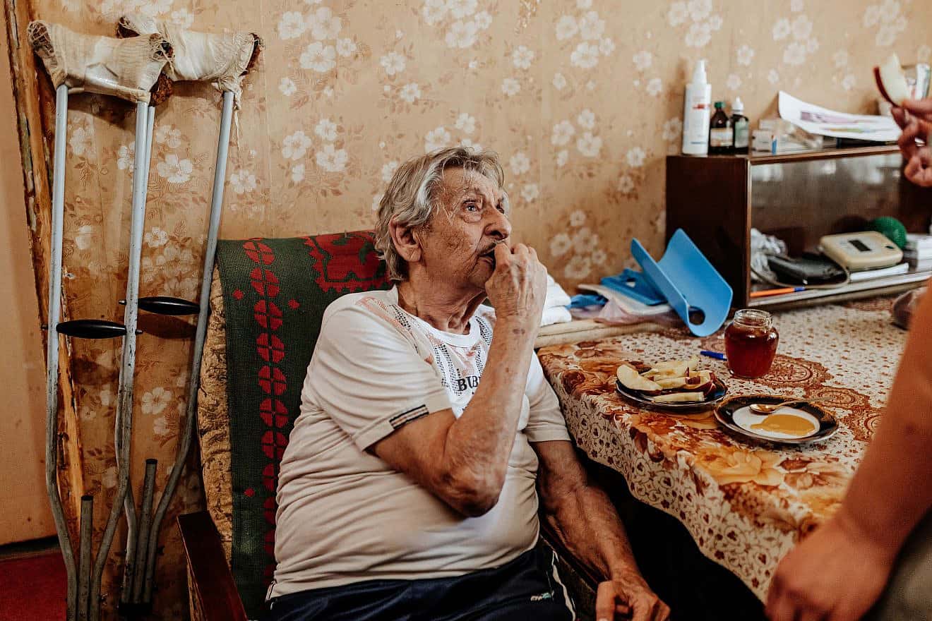 Moisey Katsman, a disabled, homebound Holocaust survivor, enjoys apples and honey delivered in advance of Rosh Hashanah 2023. He is one of thousands of the country's neediest Jews receiving New Year food packages from the American Joint Distribution Committee (JDC) in partnership with the International Fellowship of Christians and Jews, Claims Conference and Jewish Federations of North America. Photo by Misha Kovalev.