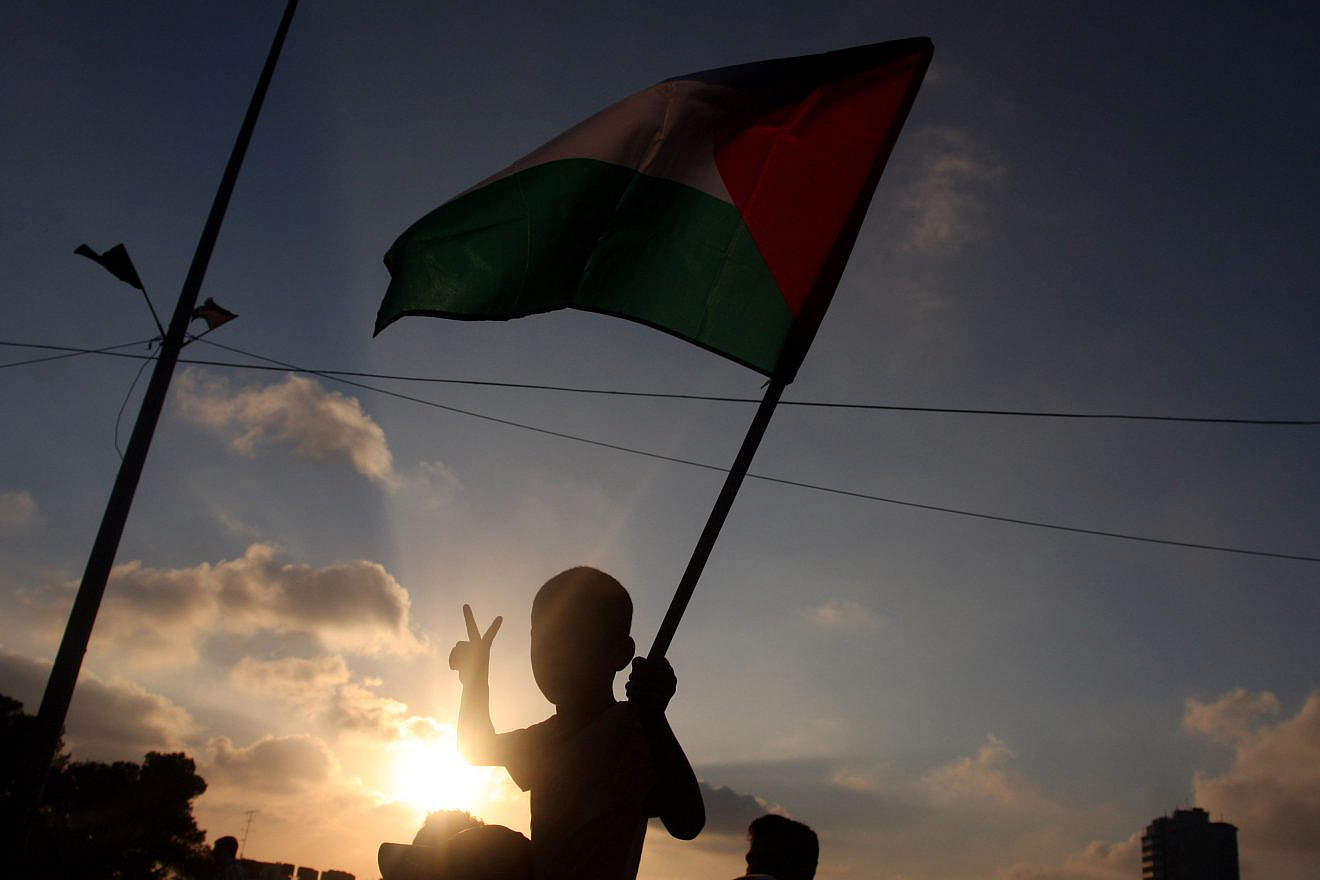 A child in the city of Ramallah holds a Palestinian national flag, while at the same time signing for peace, during a local protest against the Paris Protocol and the Oslo Accords, both key agreements that govern economic ties between Israelis and Palestinians, Sept. 11, 2012. Photo by Issam Rimawi/Flash90.