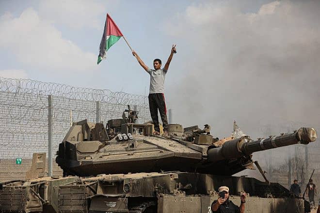Palestinians in the Gaza Strip take photos next to a burning tank on the Israeli side of the border fence with Khan Yunis on Oct. 7, 2023. Photo by Yousef Mohammed/Flash90.
