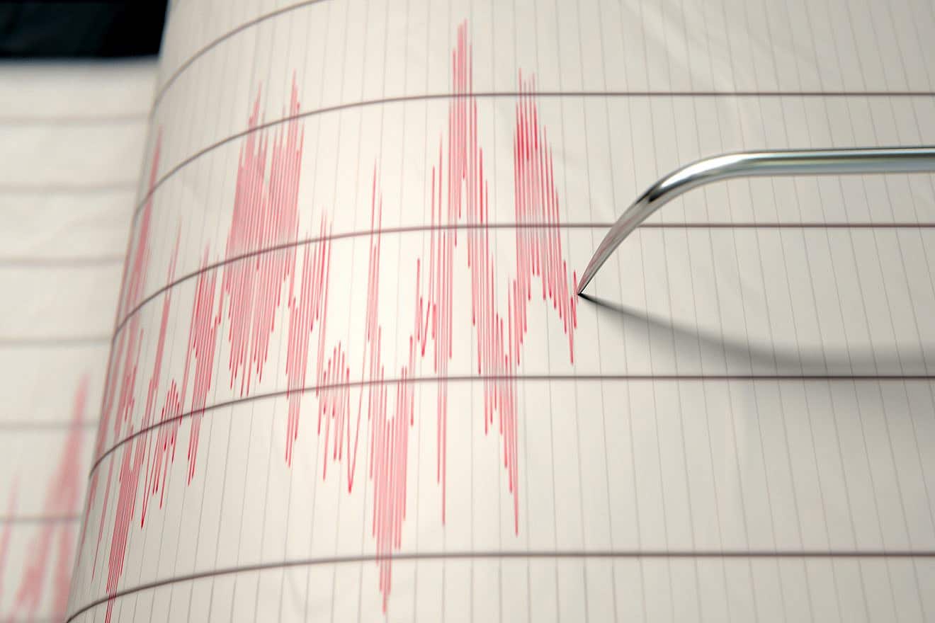 A close-up of a seismograph machine needle drawing a red line on graph paper depicting seismic and earthquake activity. Credit: Inked Pixels/Shutterstock.