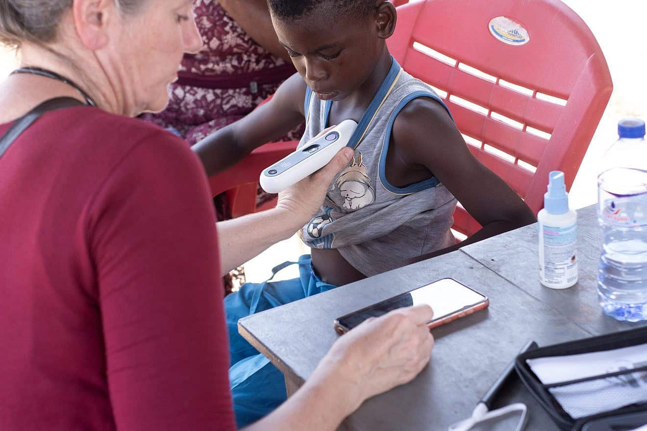 At an ImpactWell GNMC mobile clinic, Dr. Britta Budde Schwartzman examines a child using a multipurpose diagnostic tool developed by Nonagon that records the data on a smartphone for assessment by physicians on site and, if necessary, sent to specialists at a distant hospital. ImpactWell is a project of the Ruderman Family Foundation and the American Jewish Joint Distribution Committee (JDC). Photo by Ezra Asare.