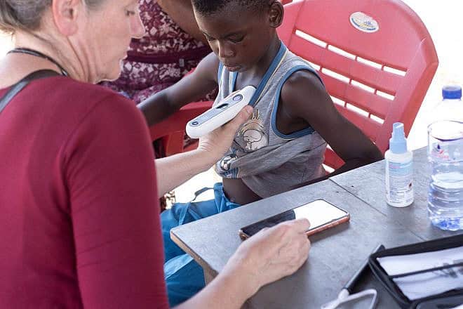 At an ImpactWell GNMC mobile clinic, Dr. Britta Budde Schwartzman examines a child using a multipurpose diagnostic tool developed by Nonagon that records the data on a smartphone for assessment by physicians on site and, if necessary, sent to specialists at a distant hospital. ImpactWell is a project of the Ruderman Family Foundation and the American Jewish Joint Distribution Committee (JDC). Photo by Ezra Asare.
