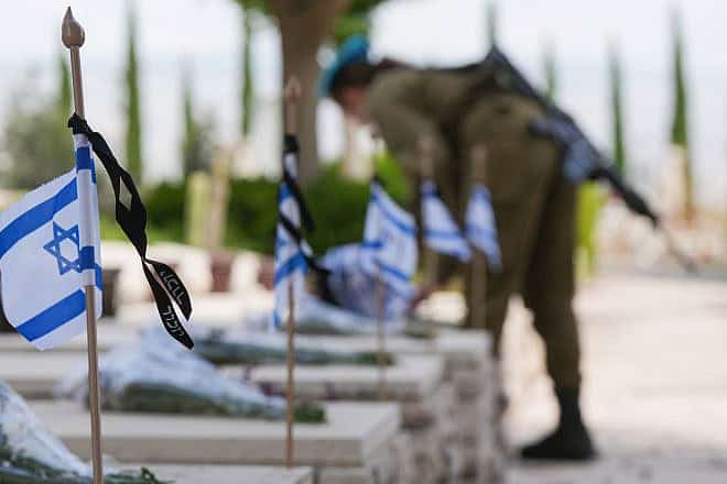 An Israeli soldier places flowers and flags on graves at the military cemetery in Kiryat Shmona on May 12, ahead of Israeli Memorial Day on May 13, 2024. Photo by Ayal Margolin/Flash90.