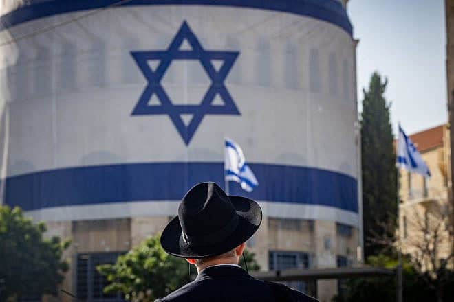 An Ultra-Orthodox Jewish man standing under a huge Israeli flag in Jerusalem, June 3, 2024. Photo by Yonatan Sindel/Flash90.