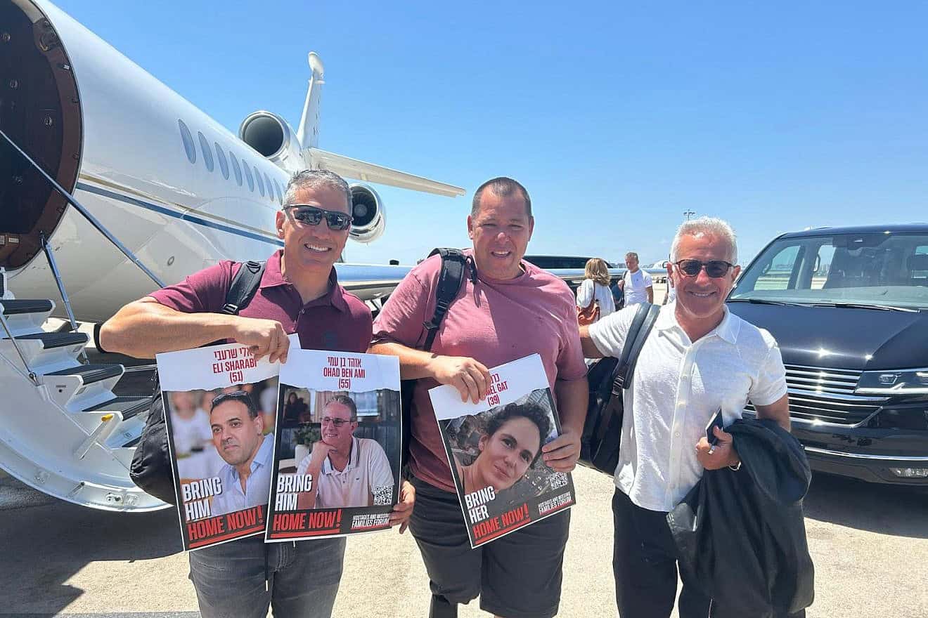 From left: Oct. 7 survivors Sharon Shevo and Avida Bachar, and philanthropist Sylvan Adams, hold posters of kidnapped Israelis from Kibbutz Be'eri as they embark on Adams's private jet en route to the Tour de France, June 2024. Photo by Amelie Botbol.