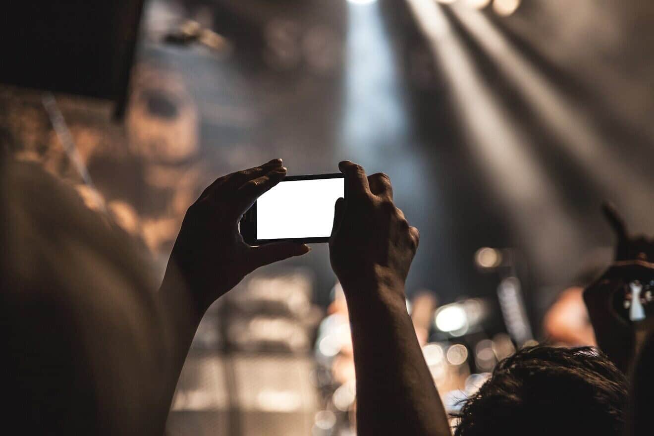 An audience member takes a photo on a smartphone in the midst of a concert crowd. Credit: SplitShire/Pixabay.