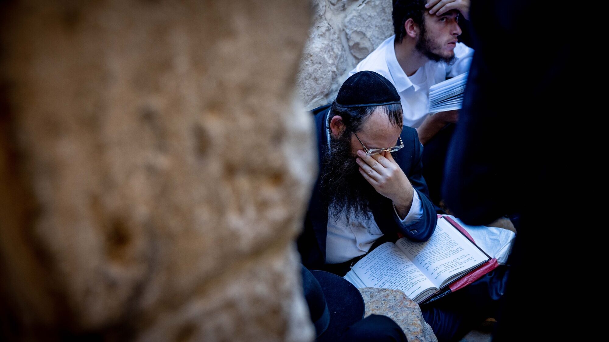 Worshippers pray sitting on the ground in mourning at the Western Wall in Jerusalem's Old City on Tisha B'Av, on July 27, 2023. Photo by Chaim Goldberg/Flash90.