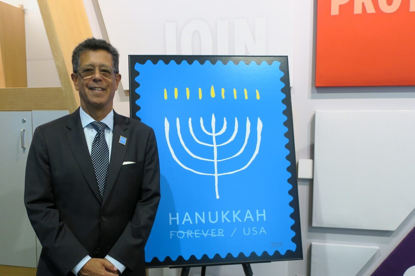 Antonio Alcalá, a designer and art director at the United States Postal Service, poses with a Chanukah stamp that he designed on Sept. 19, 2024 at the Capital Jewish Museum. Photo by Menachem Wecker.