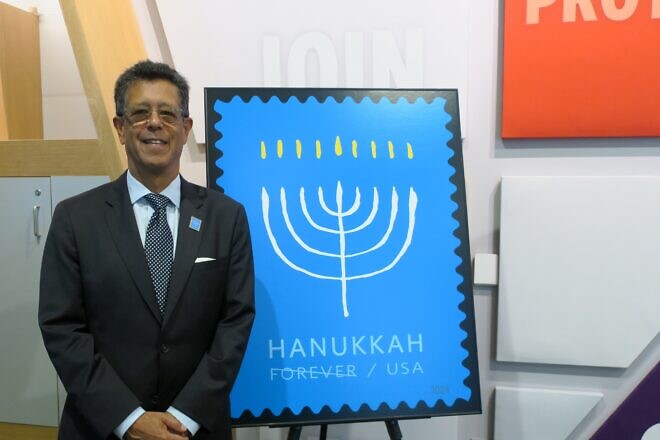 Antonio Alcalá, a designer and art director at the United States Postal Service, poses with a Chanukah stamp that he designed on Sept. 19, 2024 at the Capital Jewish Museum. Photo by Menachem Wecker.