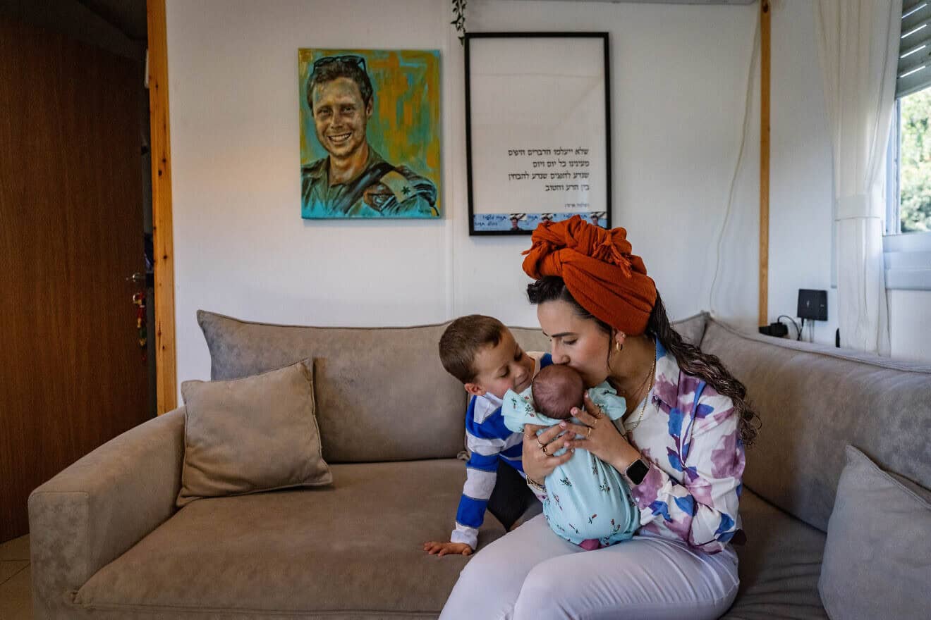 Israel Defense Forces widow Revital Shamir, her 4-year-old son and newborn baby girl sit underneath a painting of her late husband, Maj. Mordechai Shamir, at their home in Yair's Farm in Samaria, Feb. 21, 2024. Photo by Chaim Goldberg/Flash90.