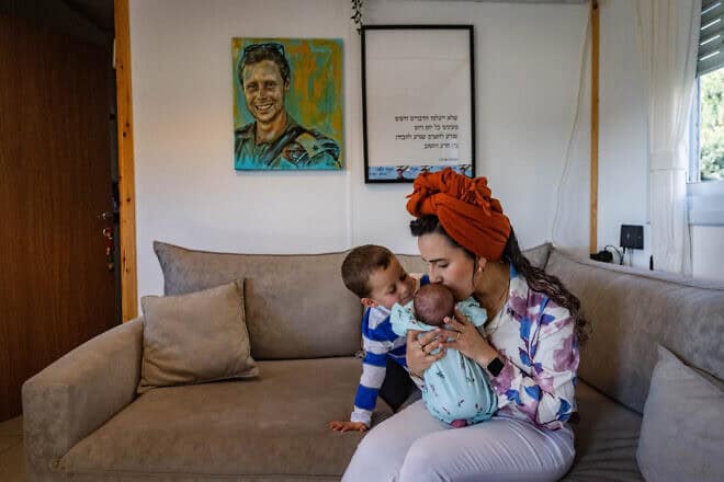 Israel Defense Forces widow Revital Shamir, her 4-year-old son and newborn baby girl sit underneath a painting of her late husband, Maj. Mordechai Shamir, at their home in Yair's Farm in Samaria, Feb. 21, 2024. Photo by Chaim Goldberg/Flash90.