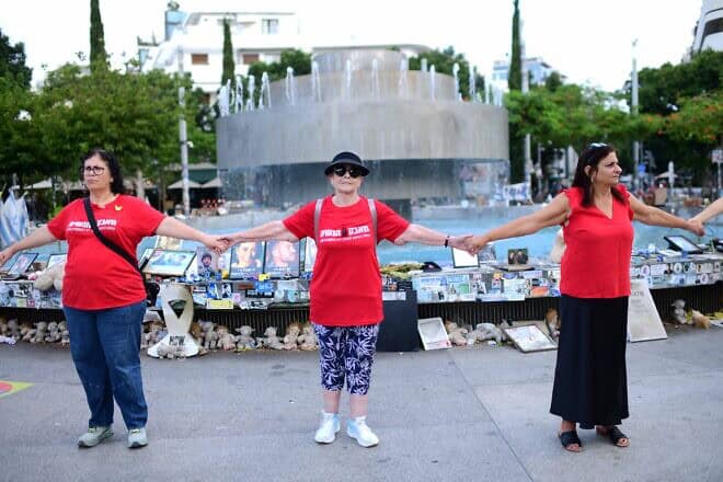 Israelis hold hands at Dizengoff Square in Tel Aviv, next to photographs of Israelis killed in the Oct. 7 massacre, on the one-year anniversary of the Hamas attack. Oct/ 7, 2024. Photo by Tomer Neubergi/Flash90.