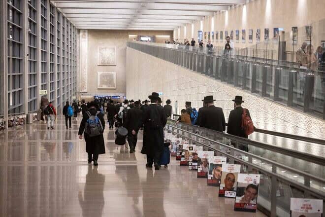 Travelers walk next to pictures of Israelis held hostage by Hamas in the Gaza Strip at Ben-Gurion International Airport, Oct. 8, 2024. Photo by Chaim Goldberg/Flash90.