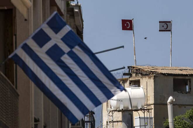 A Greek national flag (foreground) hangs on the southern side of Cyprus' divided capital Nicosia near the buffer zone, which separates the internationally recognized Republic of Cyprus and and the self-proclaimed Turkish Republic of Northern Cyprus, as flags of Turkey (center) and the TRNC (right) are seen on a Turkish military outpost on July 9, 2024. Photo by Amir Makar/AFP via Getty Images.