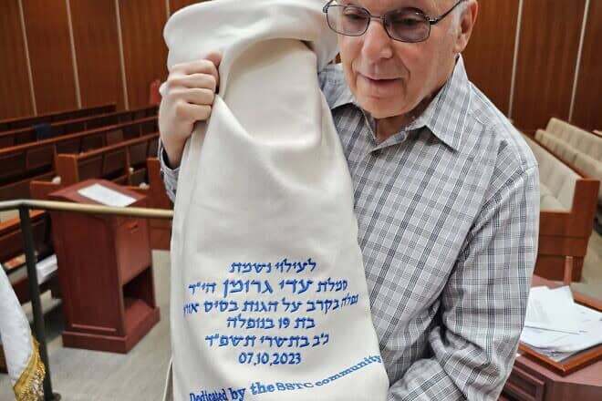 George Kafka holds a Torah with a mantle dedicated in memory of his relative Sgt. Adi Gruman, an IDF soldier who was killed on Oct. 7, 2023, given to the Modern Orthodox congregation Synagogue of the Suburban Torah Center in Livingston, N.J., through the Simchat Torah Project. Credit: Courtesy.