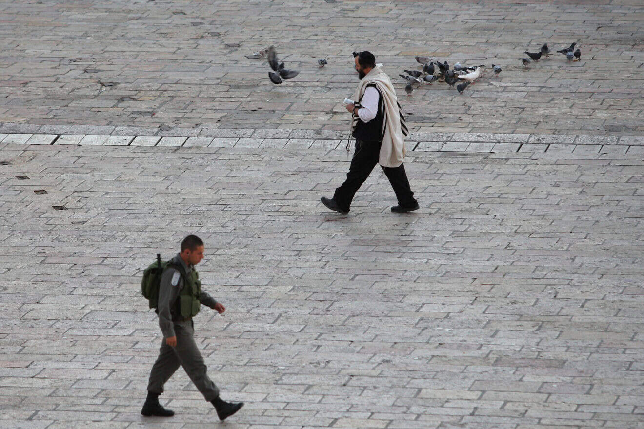 An Orthodox man walks along the Western Wall plaza, passing an Israeli soldier in the Old City of Jerusalem. Photo by Keren Freeman/Flash90.