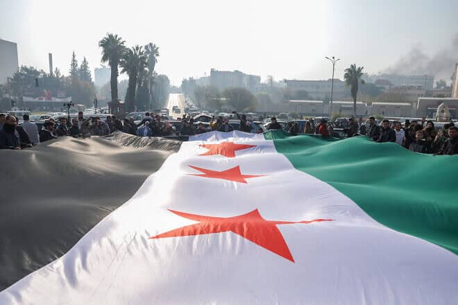 People celebrate holding a large Syrian opposition flag at Umayyad Square in Damascus, Dec. 9, 2024. Photo by Omar Haj Kadour/AFP via Getty Images.