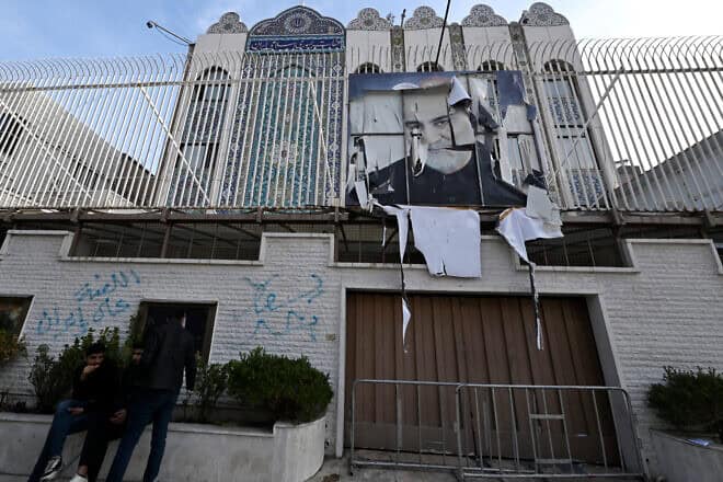 Young Syrians sit outside Iranian embassy, which was ransacked after anti-government fighters took Damascus the previous day, with a portrait of Iran's slain Revolutionary Guards commander Qassem Soleimani still hanging on its fence, in the Syrian capital on Dec. 9, 2024. Photo by Louai Beshara/AFP via Getty Images.