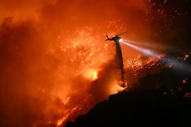 A firefighting helicopter drops water as the Palisades Fire grows near the Mandeville Canyon neighborhood and Encino, Calif., on Jan. 11, 2025. Photo by Patrick T. Fallon/AFP via Getty Images.