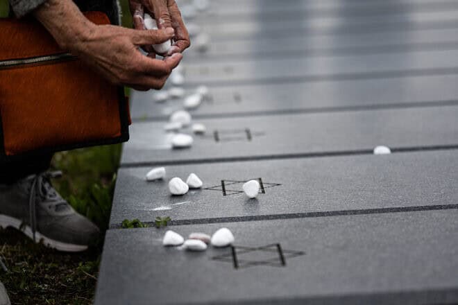 A woman places white visitation stones on a grave marker at Stuttgart Army Airfield in Filderstadt, Germany, 2023. Credit: U.S. Army USAG-S by Marcus Fichtl, public domain via Wikimedia Commons.