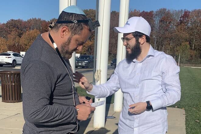 Rabbi Mendel Grossbaum helps a man put on tefillin at a rest stop before a rally for Israel, on Nov. 14, 2023. Photo by Faygie Holt.