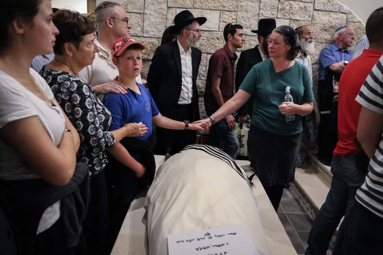 Ari Fuld's wife, Miriam, and son hold hands over his enshrouded body, wrapped in a tallit and awaiting burial at the Kfar Etzion cemetery in Judea. Photo by Gershon Elinson/Flash90.