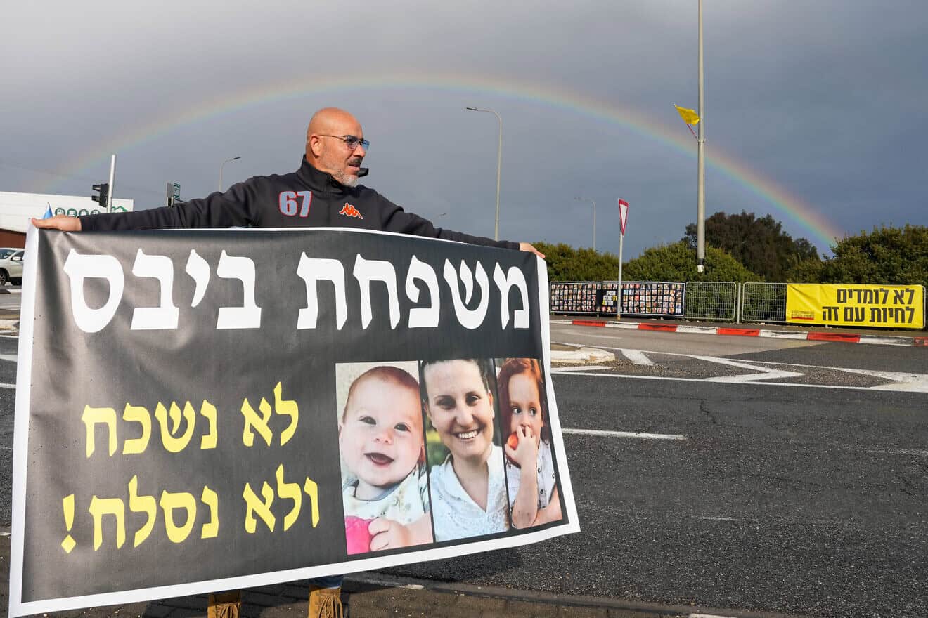 A man in northern Israel holds a banner showing members of the Bibas family—mom Shiri, and children Ariel and Kir—who were murdered by Hamas in the Gaza Strip after being taking from their home on Oct. 7, 2023, in the Hamas-led terrorist attacks in southern Israel, Feb. 20, 2025. Photo by Ayal Margolin/Flash90.