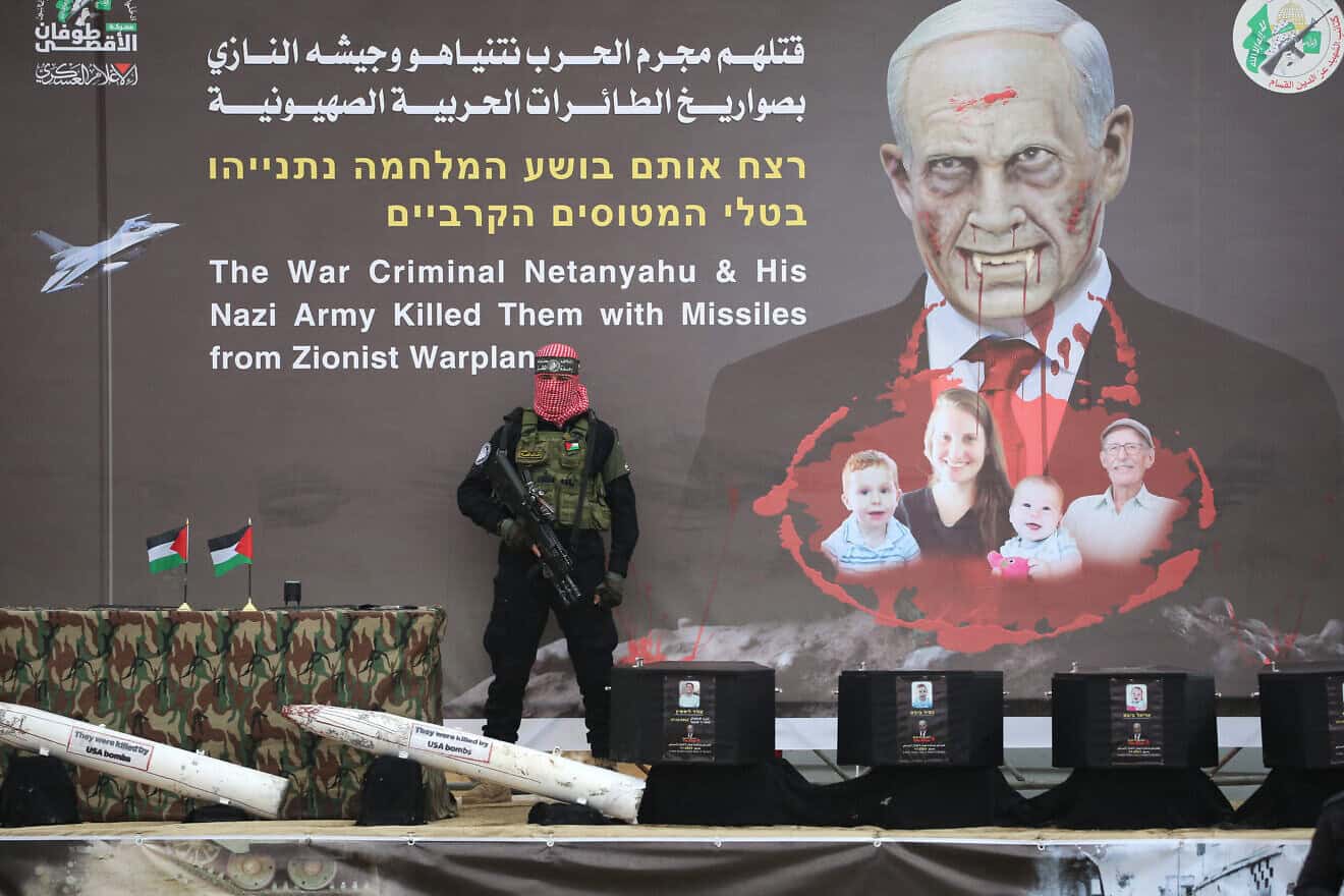 A Hamas terrorist stands in front of a banner bearing an altered portrait of Israel's prime minister and the Bibas family, on stage ahead of the handing over the bodies of four Israeli hostages in Khan Yunis in the southern Gaza Strip on Feb. 20, 2025. Photo by Eyad Baba/AFP via Getty Images.