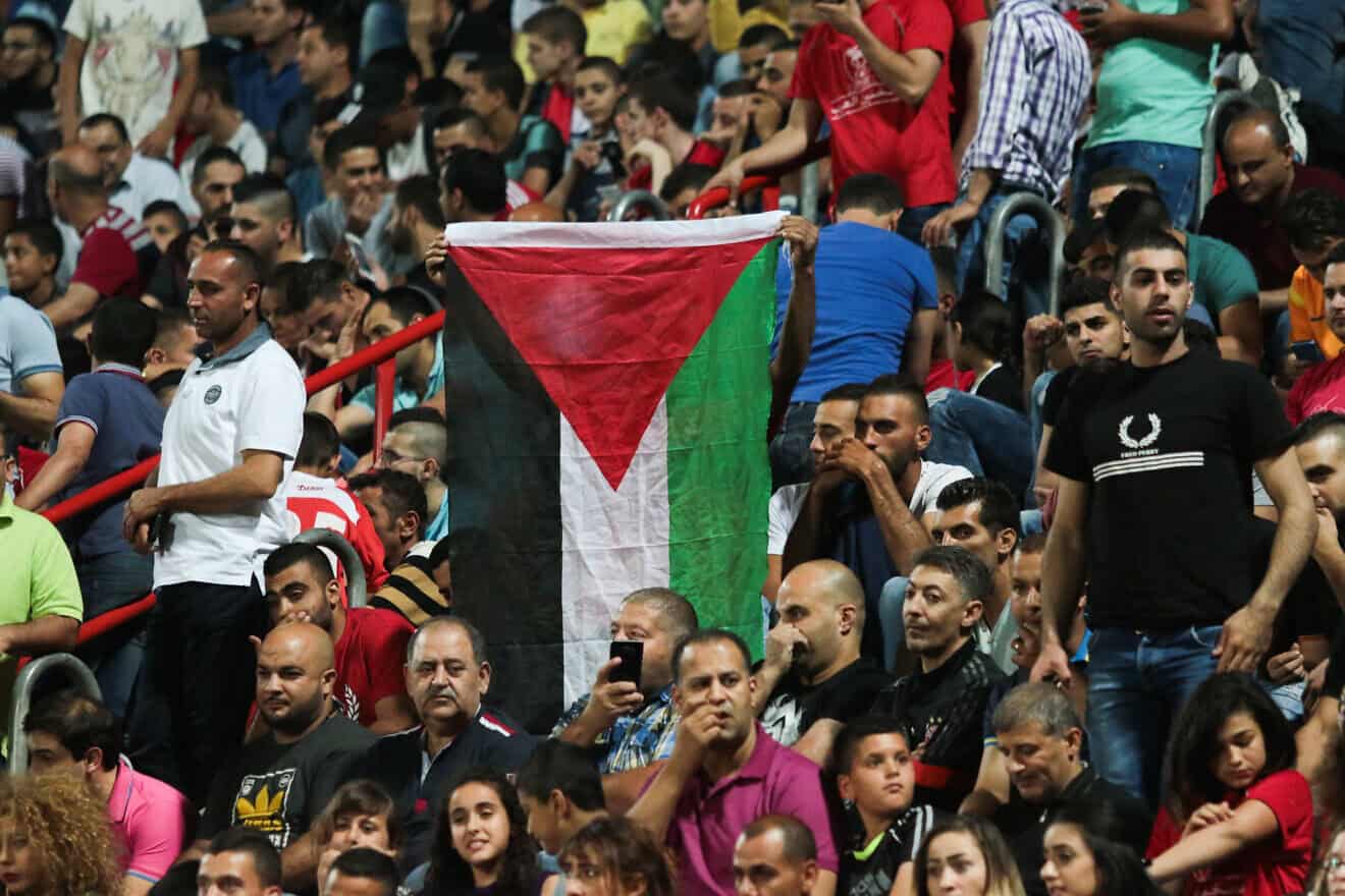 Bnei Sakhnin F.C. fans cheer alongside a PLO flag during a match against Maccabi Tel Aviv at the Doha Stadium in Sakhnin on April 25, 2016. Photo by Roy Alima/Flash90.