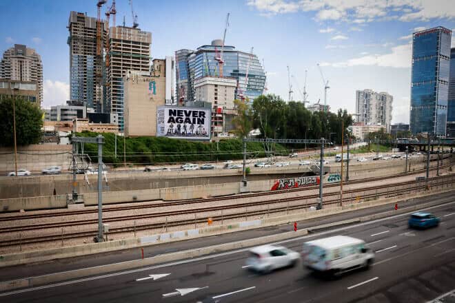 A large billboard with the words “Never Again” above the Ayalon highway in Tel Aviv, Oct. 18, 2023. Photo by Chaim Goldberg/Flash90.