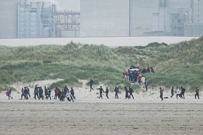 Migrants run up the dunes near Gravelines Nuclear Power Station to hide the smuggling boats from French National Police dispatched to prevent them from illegally crossing the English Channel to Britain in Gravelines, northern France, on June 12, 2023. Photo by Sameer al-Doumy/AFP via Getty Images.