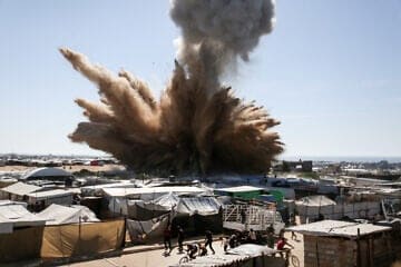 People run for cover as a plume of smoke rises above tents at a camp for displaced Palestinians in northern Khan Yunis in the southern Gaza Strip, during an Israeli strike on April 19, 2025. Photo by AFP via Getty Images.
