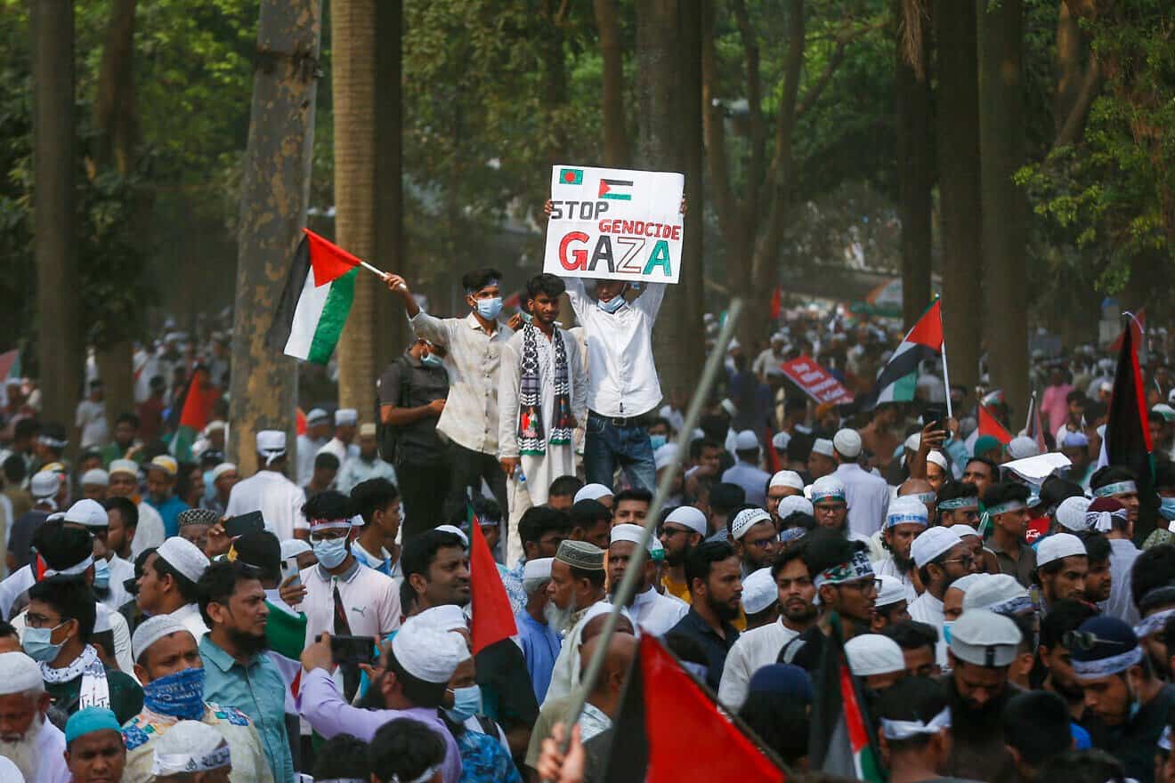 Young men stand above the crowd holding a Palestinian flag and a "Stop Genocide in Gaza" sign during a rally in Dhaka, Bangladesh on April 12, 2025. Photo by Mehedi Hasan/Middle East Images/AFP via Getty Images.