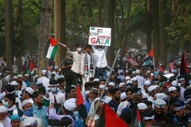 Young men stand above the crowd holding a Palestinian flag and a "Stop Genocide in Gaza" sign during a rally in Dhaka, Bangladesh on April 12, 2025. Photo by Mehedi Hasan/Middle East Images/AFP via Getty Images.